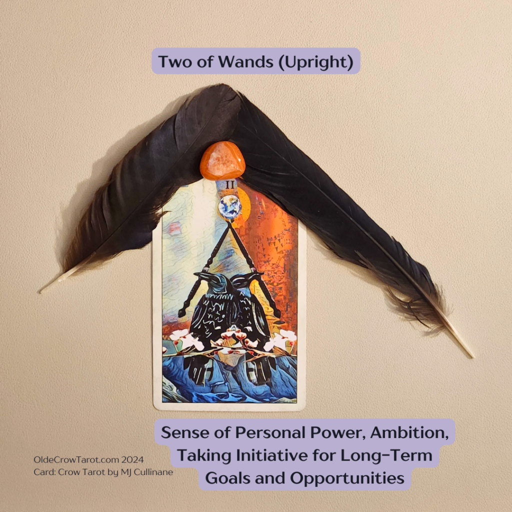 The image features a tarot card from the Crow Tarot by MJ Cullinane, named "Two of Wands (Upright)". The card is placed upright and is topped with a decorative arrangement consisting of two large feathers flanking a bright orange stone called, Carnelian. The tarot card depicts two crows standing confidently on a battlement with two wands on either side and a dynamic, fiery backdrop. Additional text on the image includes "Sense of Personal Power, Ambition, Taking Initiative for Long-Term Goals and Opportunities." The source or creator's website, "OldeCrowTarot.com 2024", is indicated at the bottom. The card defines the message of rediscovering dreams  by embracing passion and ambition on the journey of self-discovery.